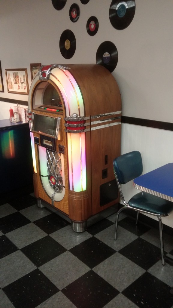 Jukebox, records on the wall, checkered floor, and a blue chair.